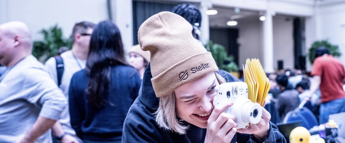 A builder in a Stellar beanie taking a photo with an instant camera at Stellar Hack Meridian in London